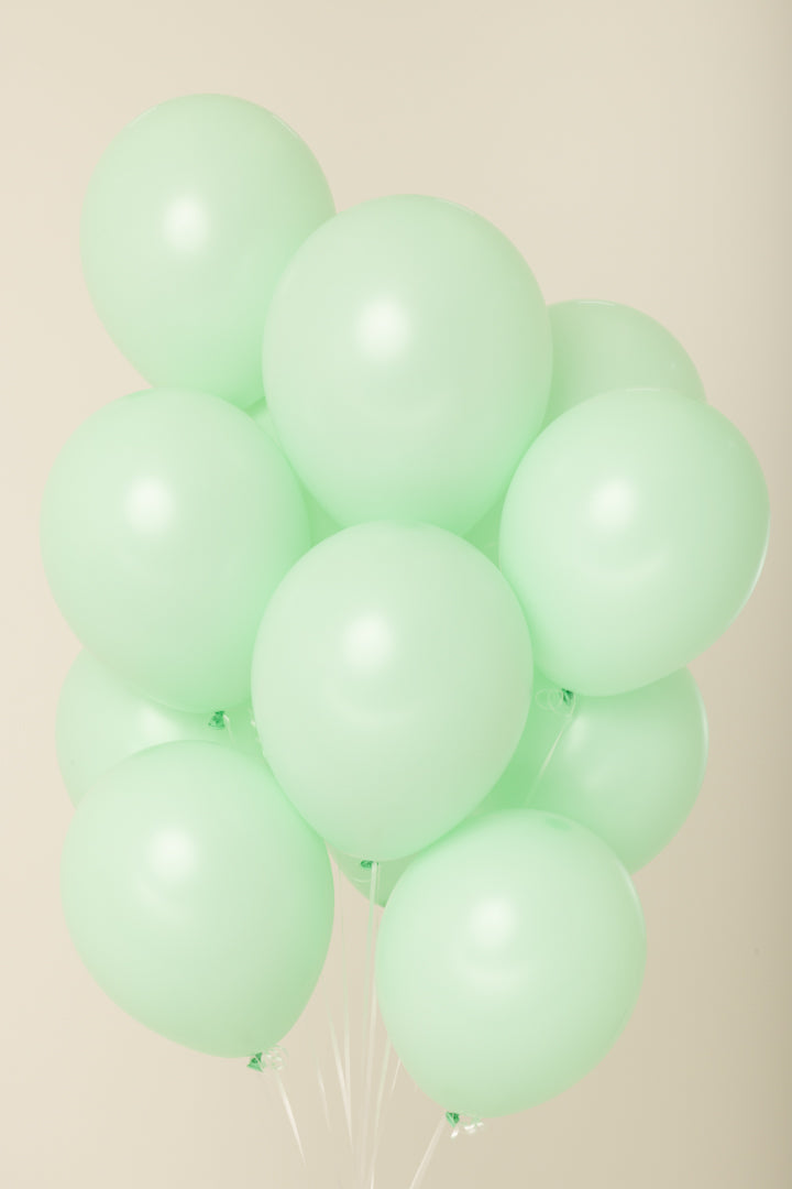 Cluster of ten light green, 11-inch latex balloons inflated with helium floating against a neutral background.