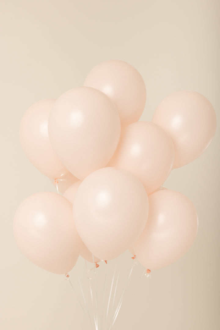Cluster of pale pink 11-inch latex helium balloons with white strings visible.