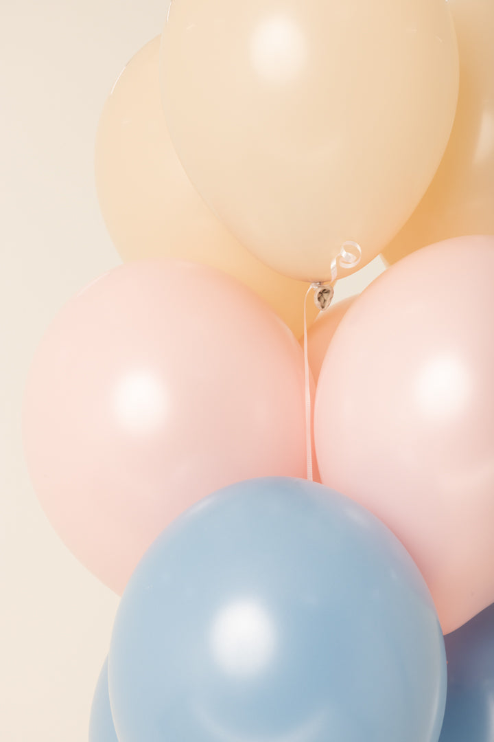 Three helium-filled latex balloons in peach, pink, and light blue, each 11 inches round.