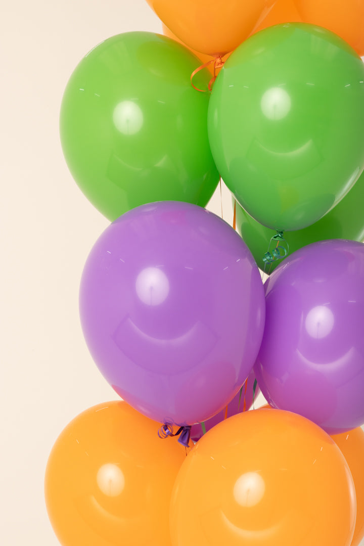 Cluster of shiny 11-inch latex balloons in green, purple, and orange colors inflated with helium.