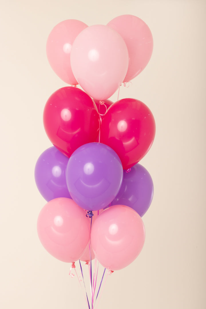 Cluster of eleven helium-inflated latex balloons in pink, red, and purple shades with ribbons.