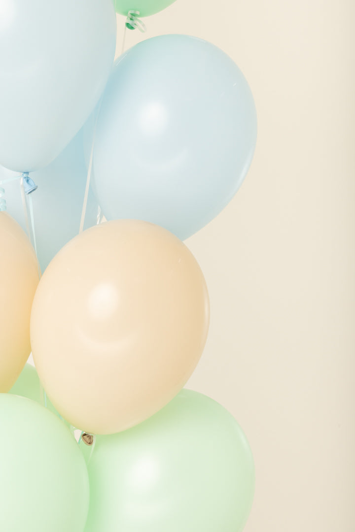 Helium-inflated round latex balloons in pale blue, beige, and light green with shiny surfaces, 11 inches tall.
