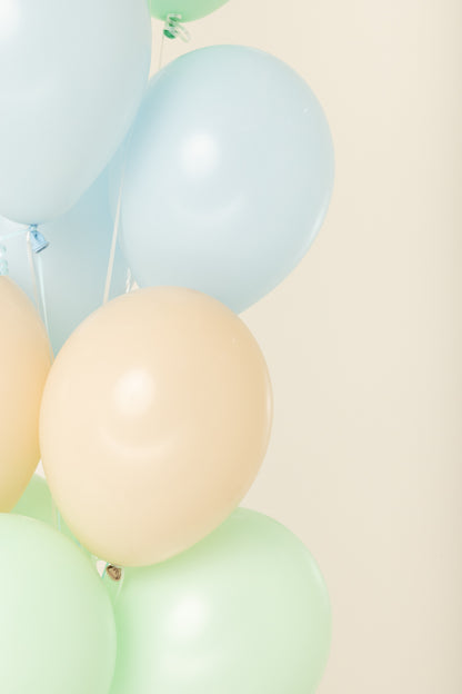 Helium-inflated round latex balloons in pale blue, beige, and light green with shiny surfaces, 11 inches tall.