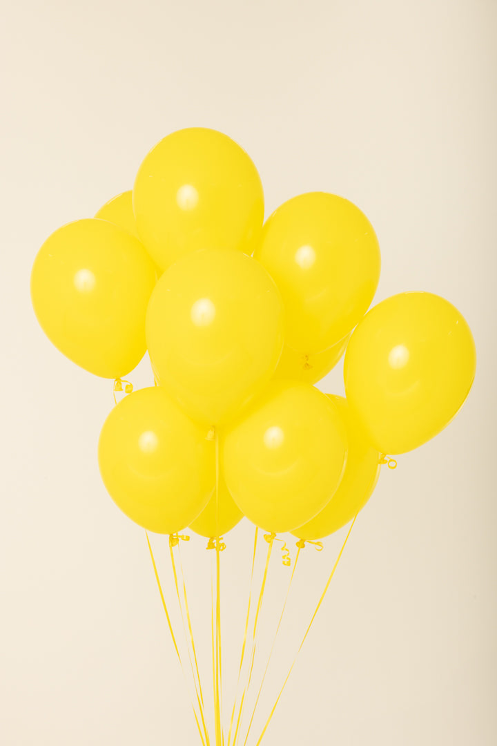 Cluster of nine bright yellow 11-inch round latex balloons inflated with helium and floating upright.