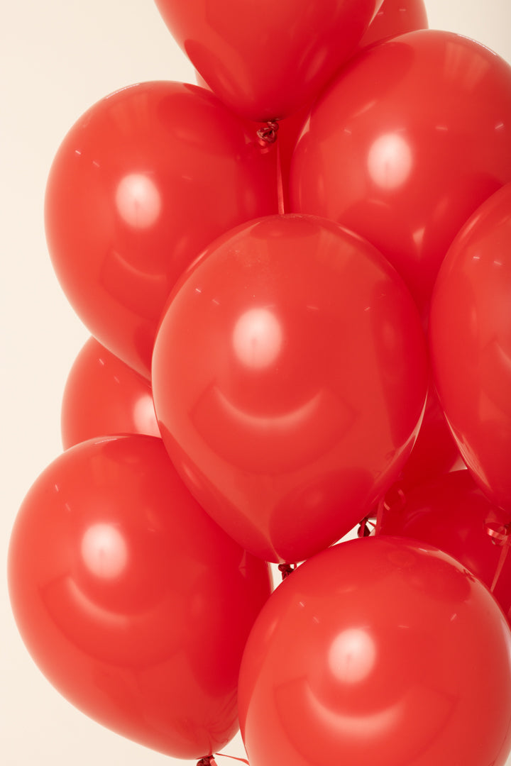 Cluster of shiny red 11-inch latex balloons inflated with helium against a light background.