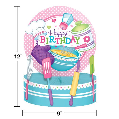 Colorful birthday centerpiece with blue cake, pink polka dot plate, chef hat, and kitchen utensils.