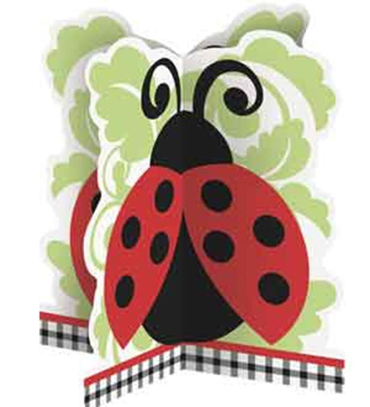 Red and black ladybug centerpiece with curled antennae and green leafy background on plaid base.