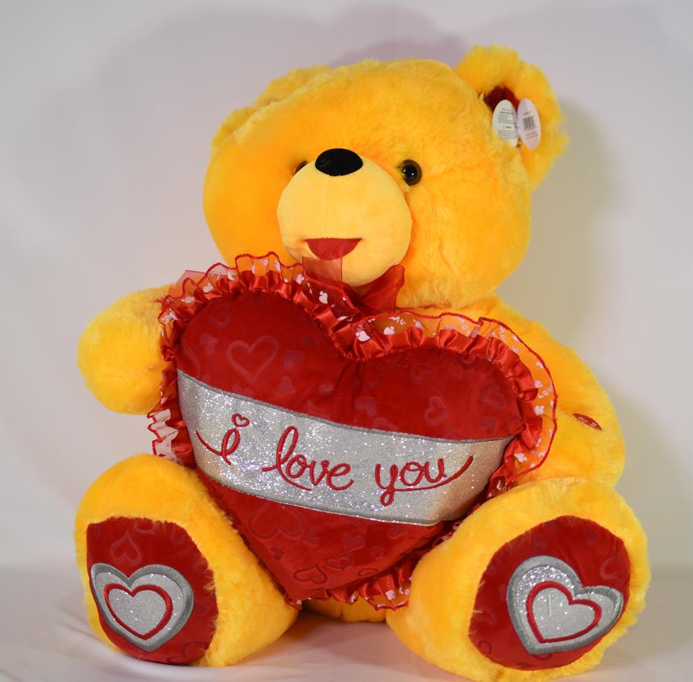 Bright yellow plush teddy bear holding a red heart pillow with "I love you" embroidered, heart details on feet.