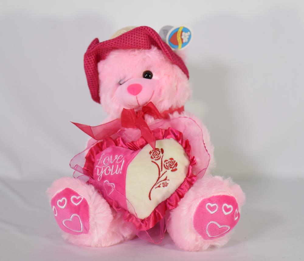 Pink plush teddy bear wearing a red hat and ribbon, holding a heart with floral design and "Love You" text.