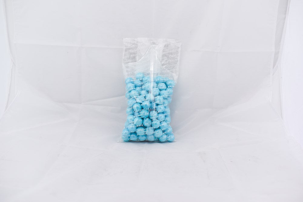 Clear plastic bag filled with small, round, shimmer-finished powder blue gumballs against a white background.