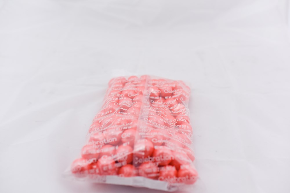 Clear plastic bag filled with round, pastel coral-colored shimmer gumballs on a white background.