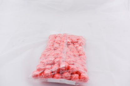 Clear plastic bag filled with round, pastel coral-colored shimmer gumballs on a white background.