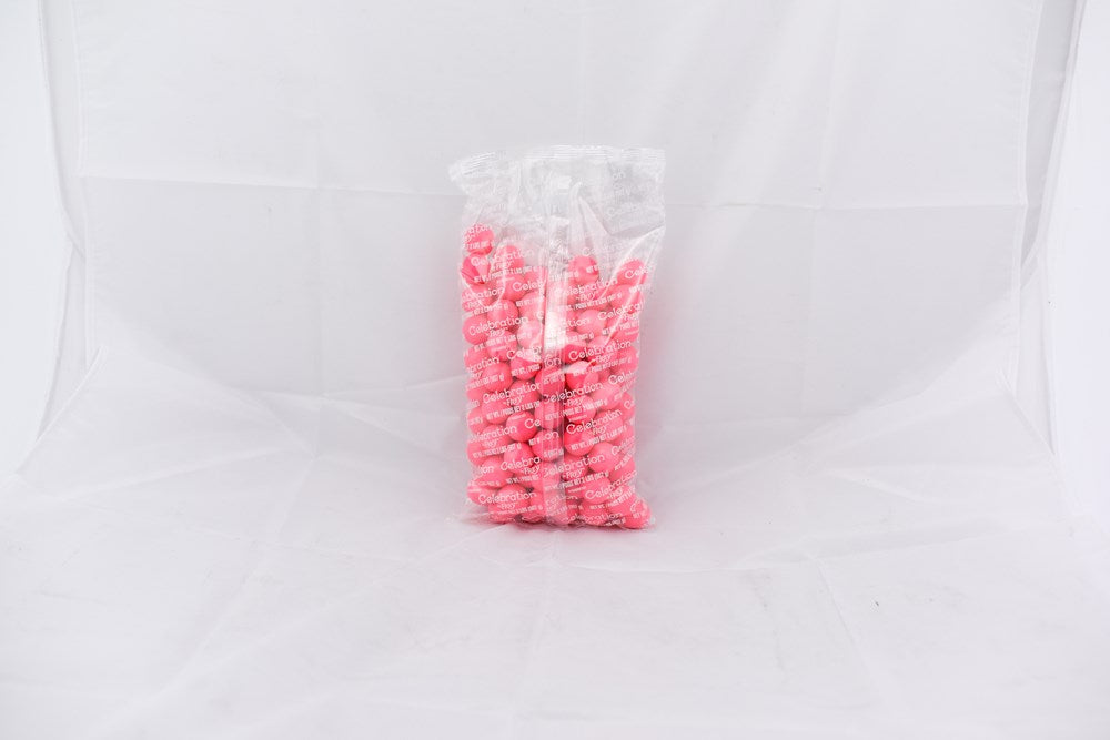 Clear plastic bag filled with small round pink gumballs against a white background.