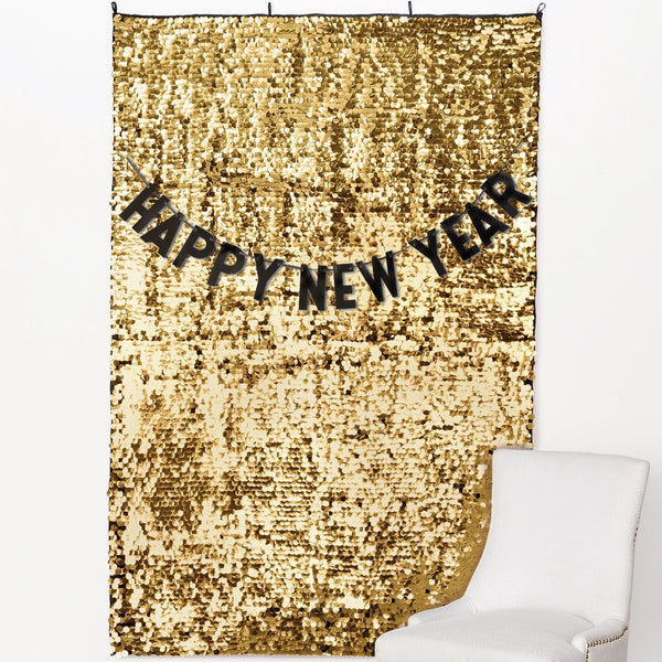 Gold sequin backdrop with black "Happy New Year" banner in bold letters.