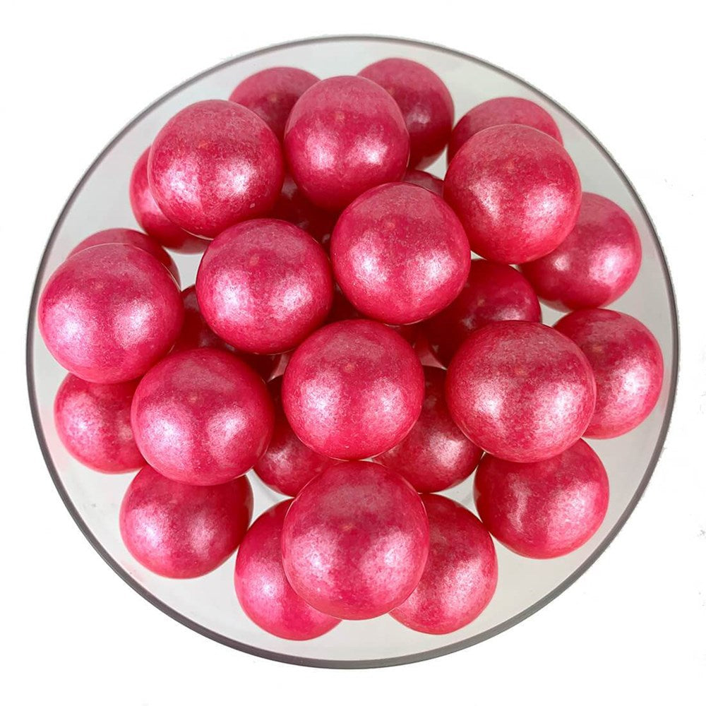 Glossy bright pink spherical gumballs with a shimmering finish arranged in a clear bowl.