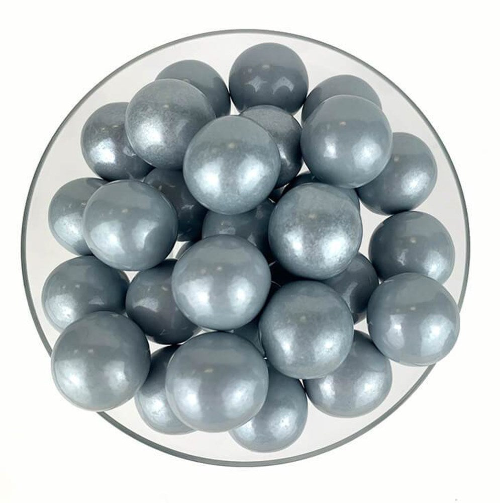 Glossy silver spherical gumballs with a smooth, shiny surface piled on a white plate.