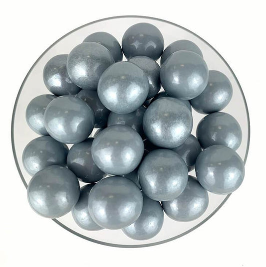 Glossy silver spherical gumballs with a smooth, shiny surface piled on a white plate.