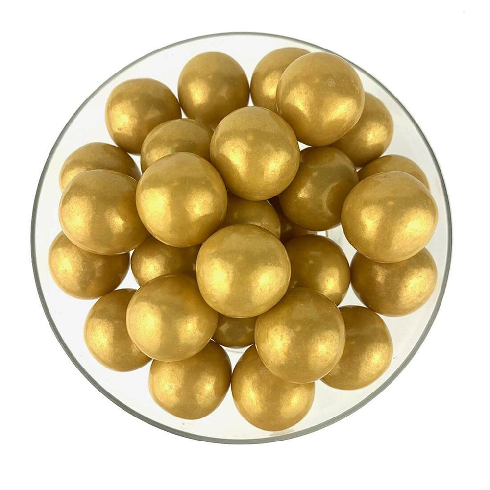 Glossy gold spherical gumballs with a smooth, shiny surface in a clear round bowl.
