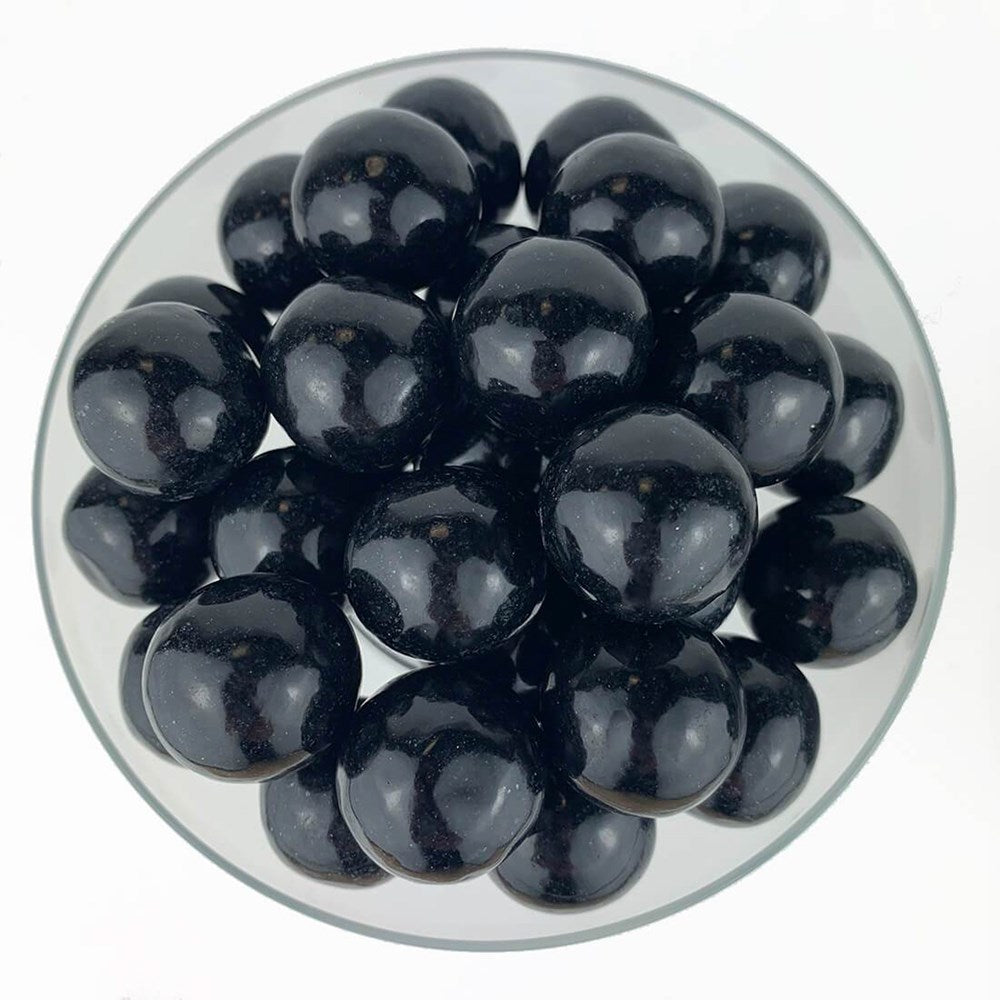 Shiny black round gumballs clustered in a clear bowl against a white background.