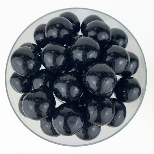 Shiny black round gumballs clustered in a clear bowl against a white background.