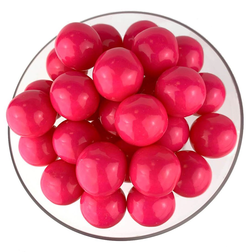 Bright pink glossy round gumballs clustered in a clear bowl.