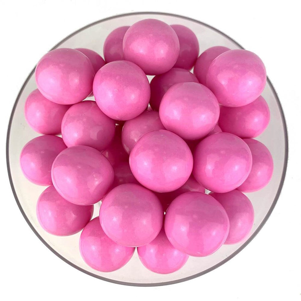 Glossy light pink round gumballs piled in a clear bowl.