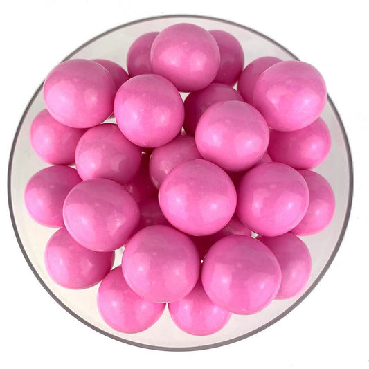 Glossy light pink round gumballs piled in a clear bowl.