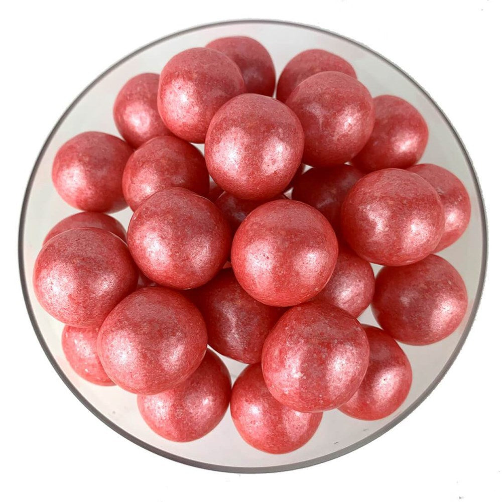 Round rose gold gumballs with a shimmering, glossy finish piled in a clear bowl.