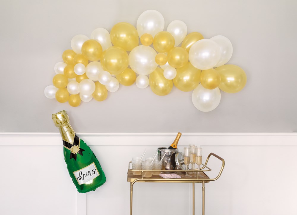 Gold and white latex balloon garland with transparent balloons, above a gold bar cart holding a champagne bottle cooler,.