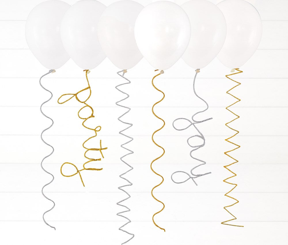 White helium balloons with silver and gold spiral pipe cleaner tails spelling out "party" and "wow" in cursive letters.