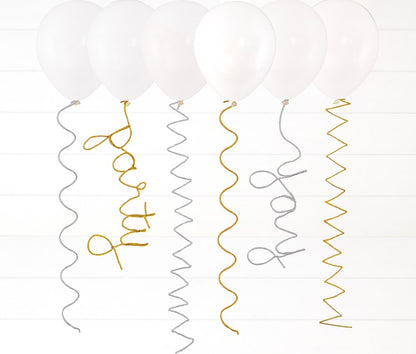 White helium balloons with silver and gold spiral pipe cleaner tails spelling out "party" and "wow" in cursive letters.