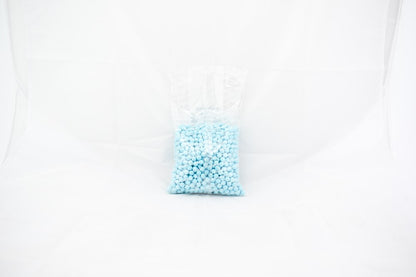 Clear plastic bag filled with small, round, powder blue beads or pellets against a white background.