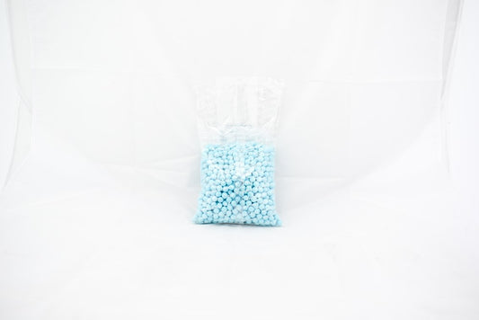 Clear plastic bag filled with small, round, powder blue beads or pellets against a white background.