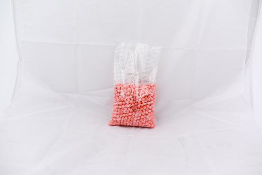 Clear plastic bag with small round coral-colored pellets inside against a white background.