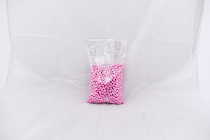 Clear plastic bag filled with small light pink round pellets on a white background.