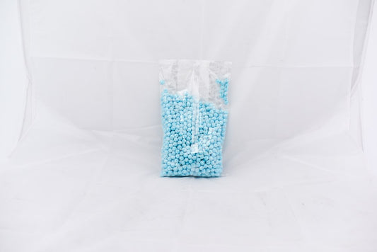 Clear plastic bag filled with small light blue powder pellets, standing upright on a white surface.