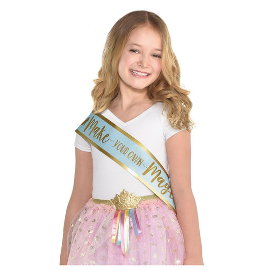 Gold satin birthday sash with "Make your own Magic" text in glitter and multicolored ribbon tails worn over white t-shirt.