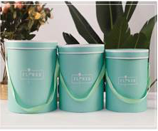 Set of three round green gift boxes with matching lids and rope handles in varying sizes.