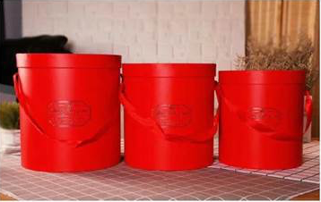 Set of three red round gift boxes with rope handles, varying in size, embossed details on front.