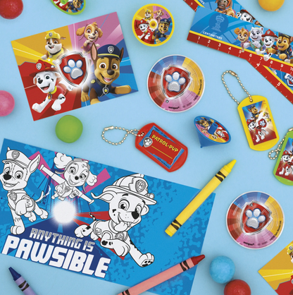 Assorted Paw Patrol party favors including yellow and blue badges, red and blue stickers, colorful candies, and crayons with