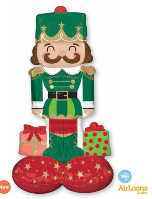 Green and red foil nutcracker balloon with gold star details and two wrapped Christmas gifts at its feet.