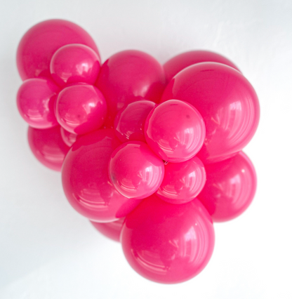 Cluster of shiny hot pink latex balloons in varying sizes inflated and arranged against a white background.