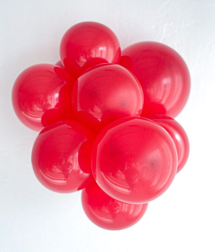 Cluster of shiny, bright red 11-inch latex balloons inflated and tightly grouped together.