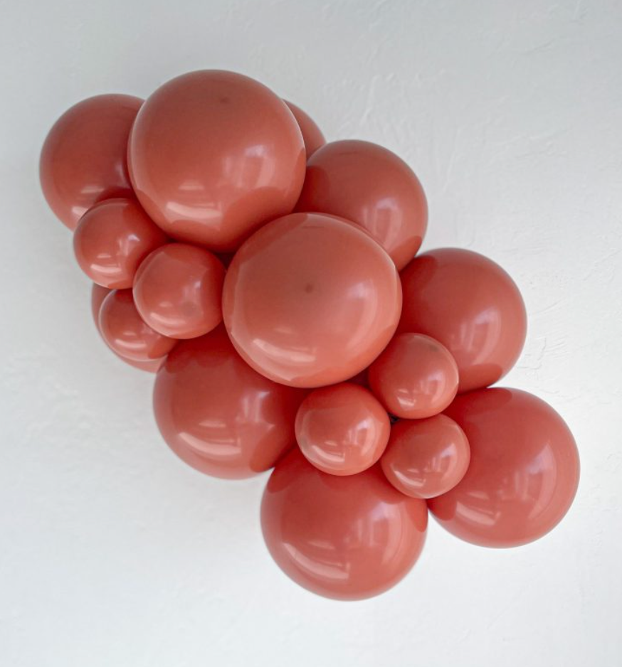 Cluster of round burnt orange latex balloons in various sizes arranged against a white background.