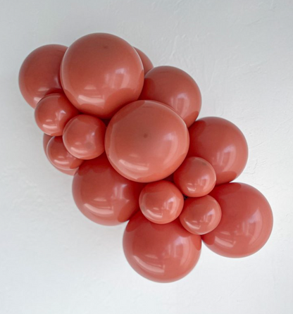 Cluster of round burnt orange latex balloons in various sizes arranged against a white background.
