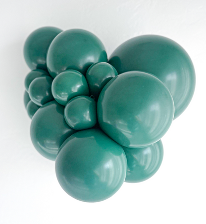 Cluster of shiny dark green latex balloons in various sizes arranged closely together against a white background.