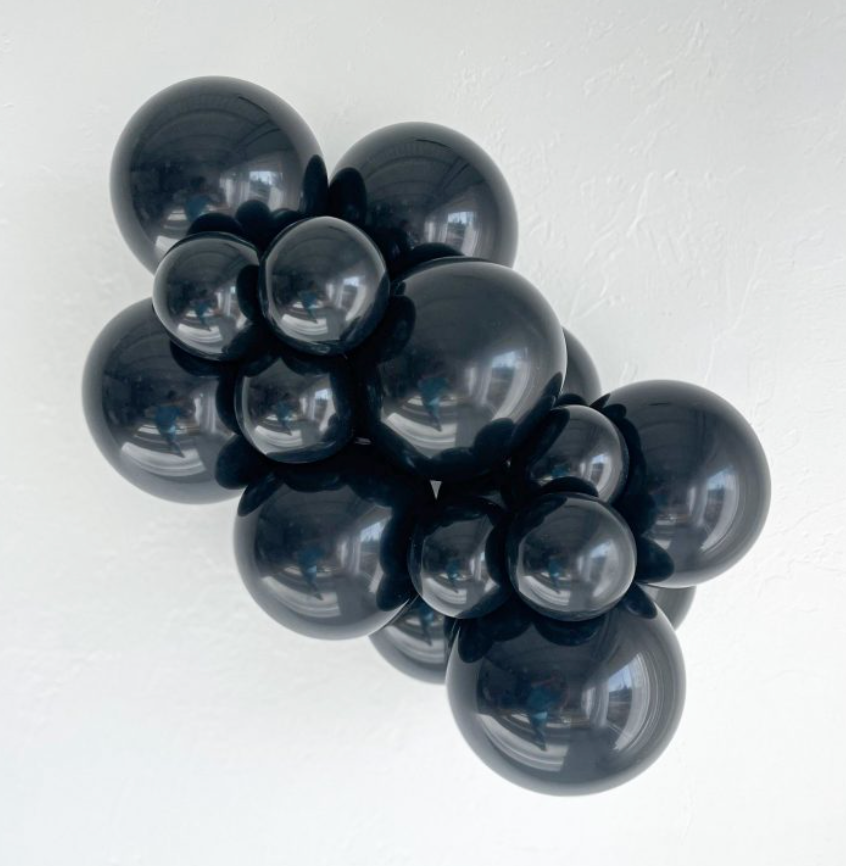 Cluster of glossy black latex balloons in various sizes, inflated and arranged closely together.